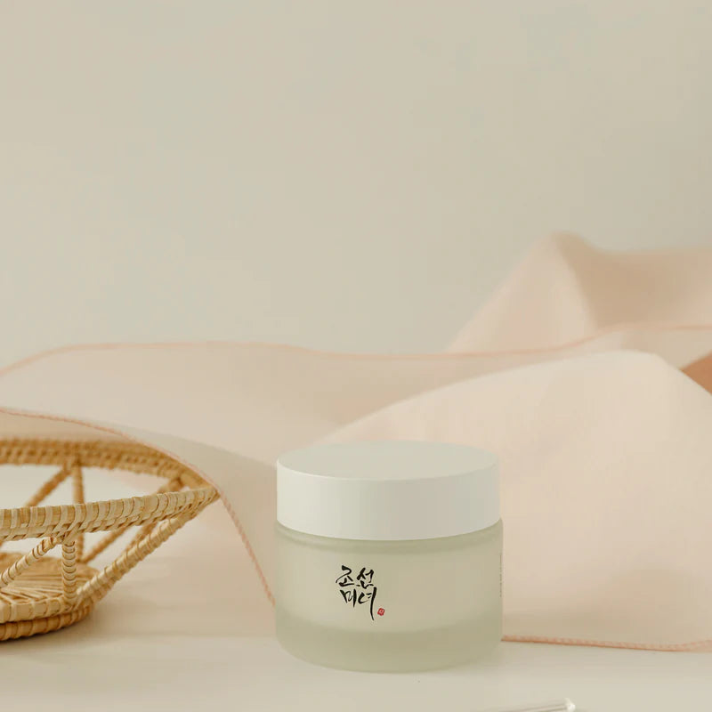 Beauty of Joseon Dynasty Cream i en mörk beige bakgrund med en korg och silkesnäsduk bredvid.