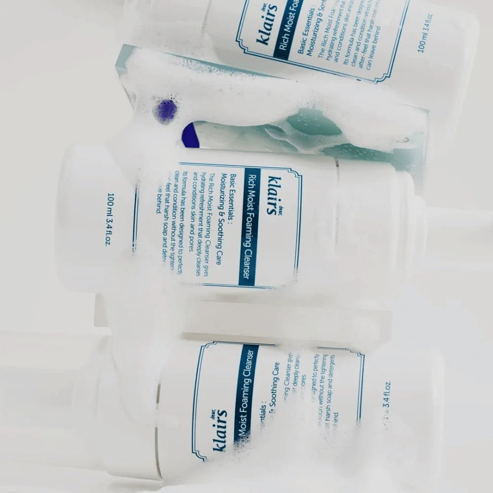 Flera Klairs Rich Moist Foaming Cleanser på en vit bakgrund, omgivna av skum. 