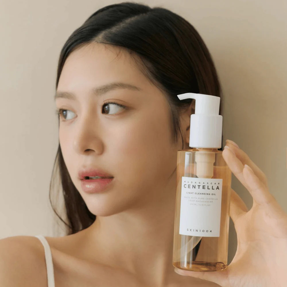 En kvinna som håller SKIN1004 Madagascar Centella Light Cleansing Oil vid sitt ansikte.