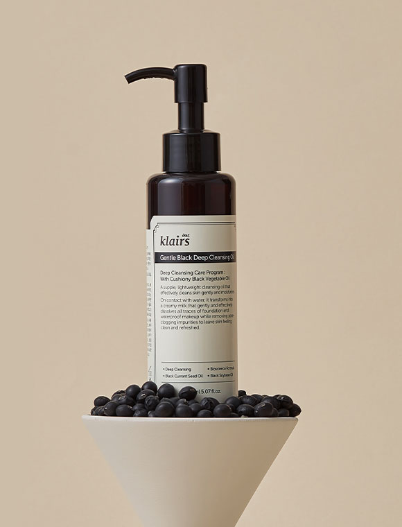 Klairs Gentle Black Deep Cleansing Oil stående på en skål med bönor mot en beige bakgrund.